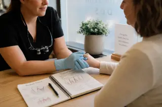 Dental professional’s gloved hands reassuringly holding a patient’s hand on a desk with treatment notes, in warm natural light