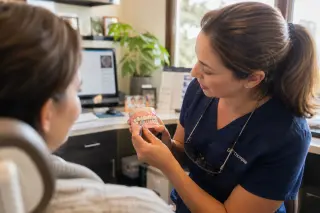 Dentist demonstrating interdental brushing with a model to a patient in a softly lit, authentic dental office
