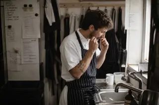 Chef in restaurant staff room discreetly using dental floss, captured naturally in a quiet moment amid a busy work environment.