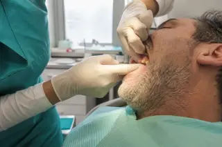 Dental professional examining a patient's gums in a softly lit, authentic clinic with a focus on the hands and subtle gum inflammation.