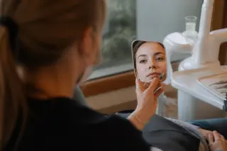 Dentist’s hand holding a mirror reflecting patient’s attentive eyes in a softly lit, welcoming dental office, capturing a moment of trust and care.