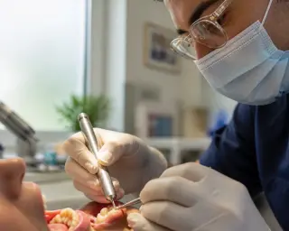 Dentist's hands delicately working on a tooth under soft natural light, with a warm, authentic clinic background and a focused professional in the blurred distance.