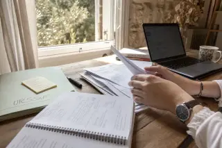 Osteopath's hands sorting paperwork on a wooden desk in a sunlit Provence office, with subtle local touches visible.