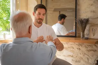 A senior patient and an osteopath in a naturally lit Provence consultation room, focusing on a subtle, attentive demonstration, with warm tones and authentic local details.